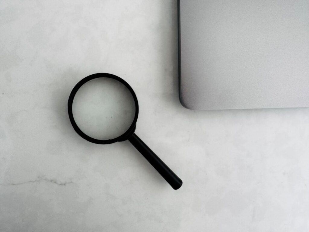 Magnifying glass next to a laptop, representing SEO search visibility